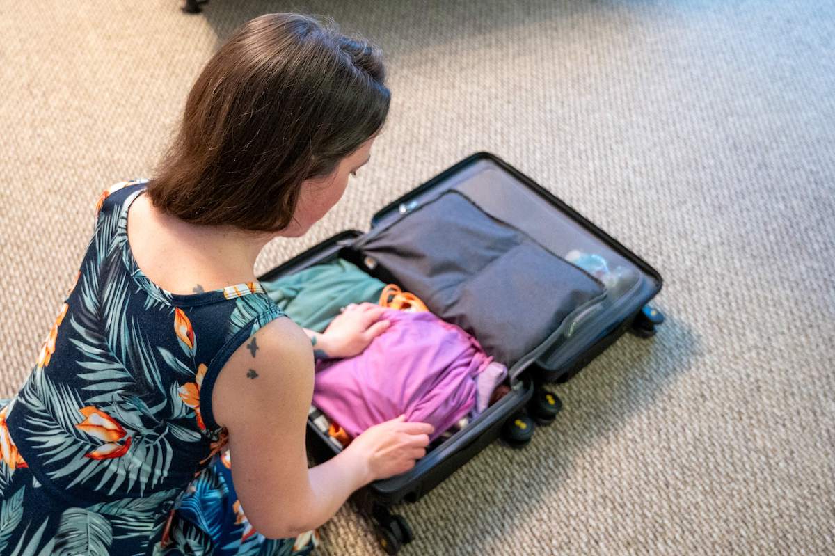 Woman packing a LEVEL8 Luminous Textured carry-on suitcase to prepare for upcoming travel