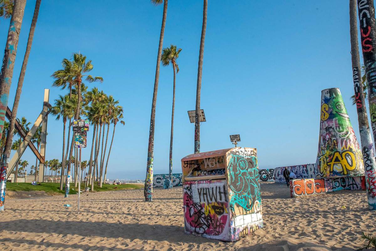 palm trees and garbage cans covered in colorful graffiti on Venice Beach in Los Angeles, California