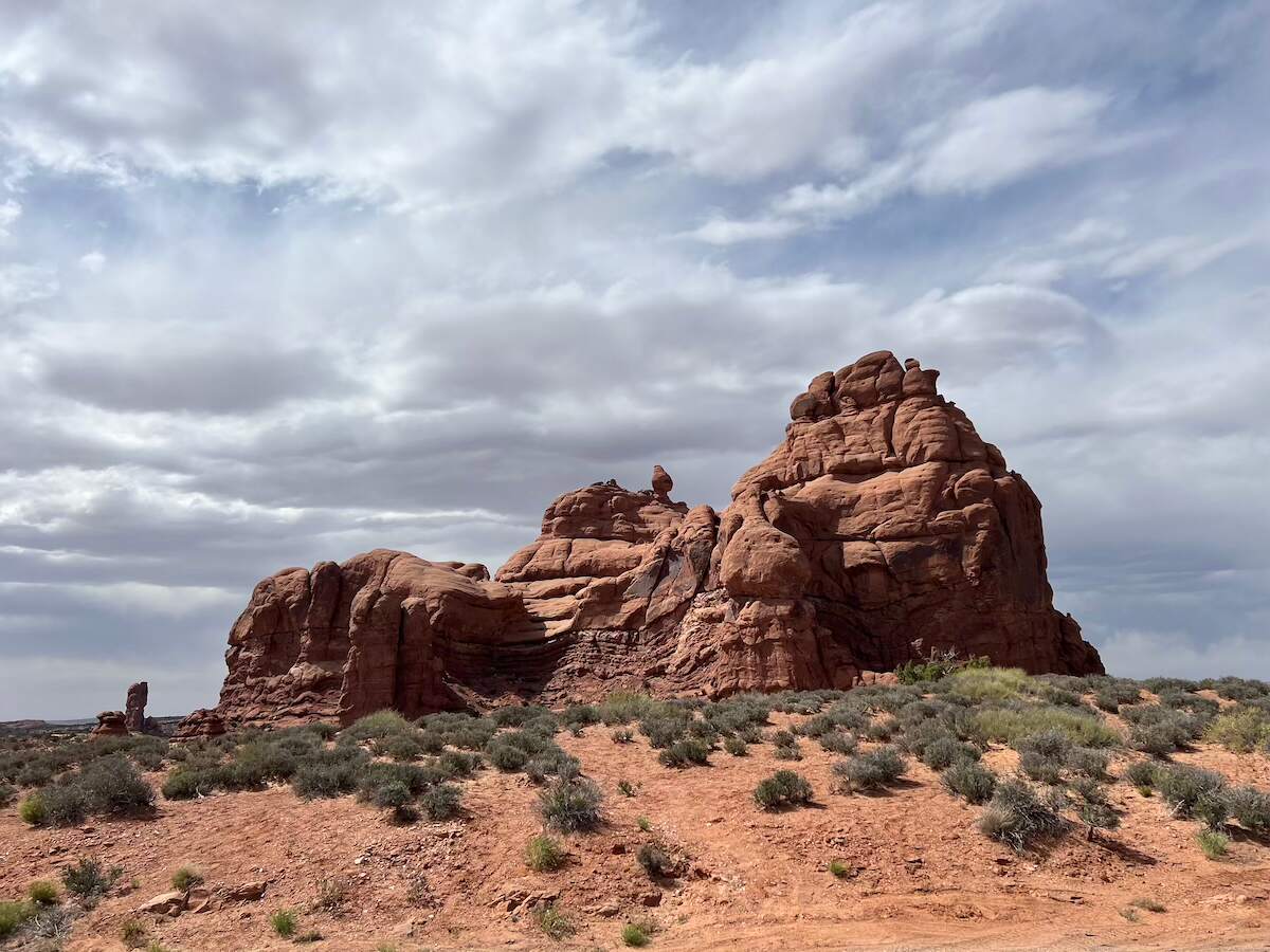 Red rock formations and sparse vegetation under a partly cloudy sky in Arches National Park. A unique and picturesque road trip destination from Denver, Colorado.