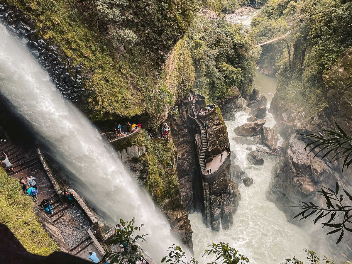 overheard view of the enormous Pailon del Diablo Waterfall gushing water next to a winding staircase in Baños