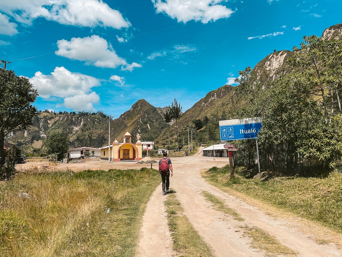 solo traveler walking through one of the small towns during the Quilotoa Loop trek in Ecuador, with charming local buildings and scenic mountainous landscapes in the background, showcasing the cultural and natural beauty of this Ecuador itinerary.