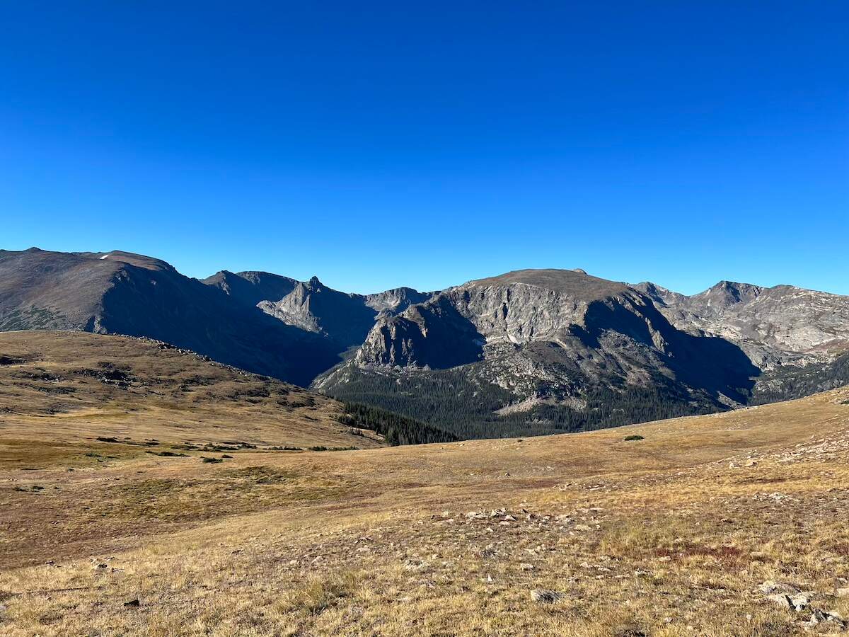 Scenic view of the Rocky Mountain National Park with rolling hills in the foreground and rugged mountain peaks under a clear blue sky. Best road trips from Denver, Colorado.