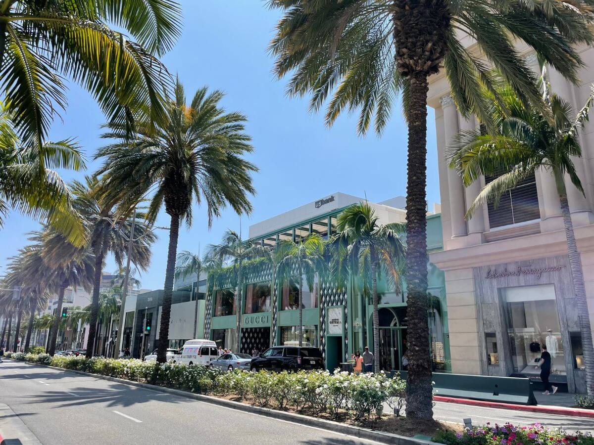 A sun-drenched view of Rodeo Drive in Los Angeles, California, showcasing its luxurious boutiques and designer storefronts. Palm trees line the iconic street, adding a touch of California charm to the upscale shopping district.