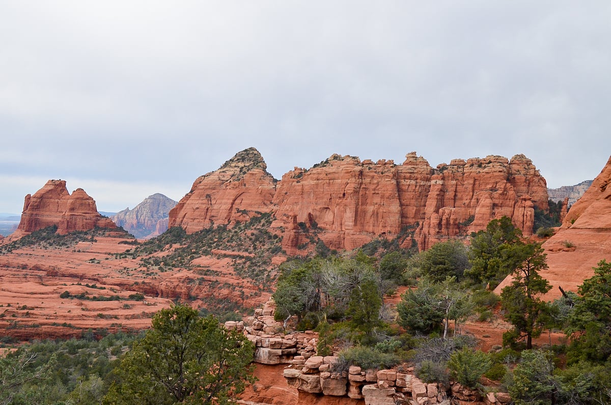 Stunning red rock formations and green vegetation under a cloudy sky in Sedona. A beautiful and popular road trip destination from Denver, Colorado.