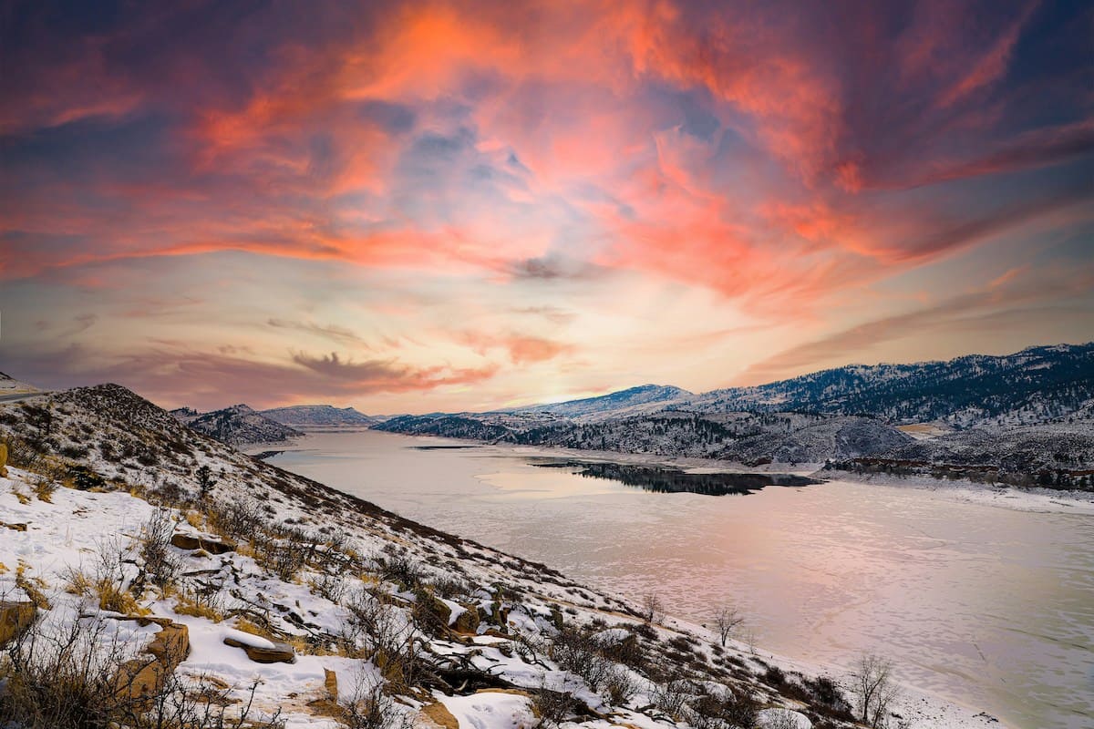 Stunning sunrise over the snow-covered landscape of Horsetooth Reservoir near Fort Collins, with vibrant pink and orange clouds reflecting on the calm water. An unforgettable road trip destination from Denver, Colorado.