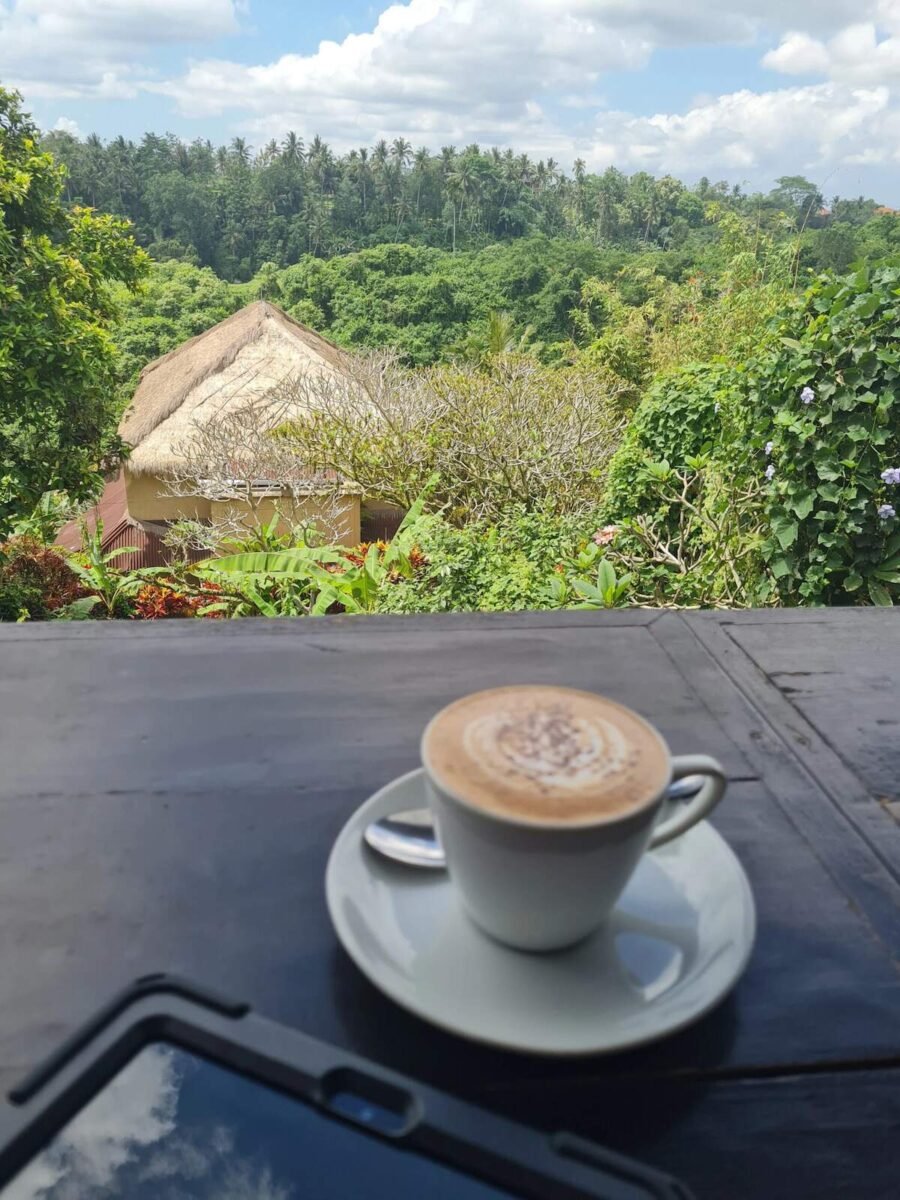 Cup of coffee with a stunning view of lush greenery and traditional thatched-roof buildings in Ubud, Bali
