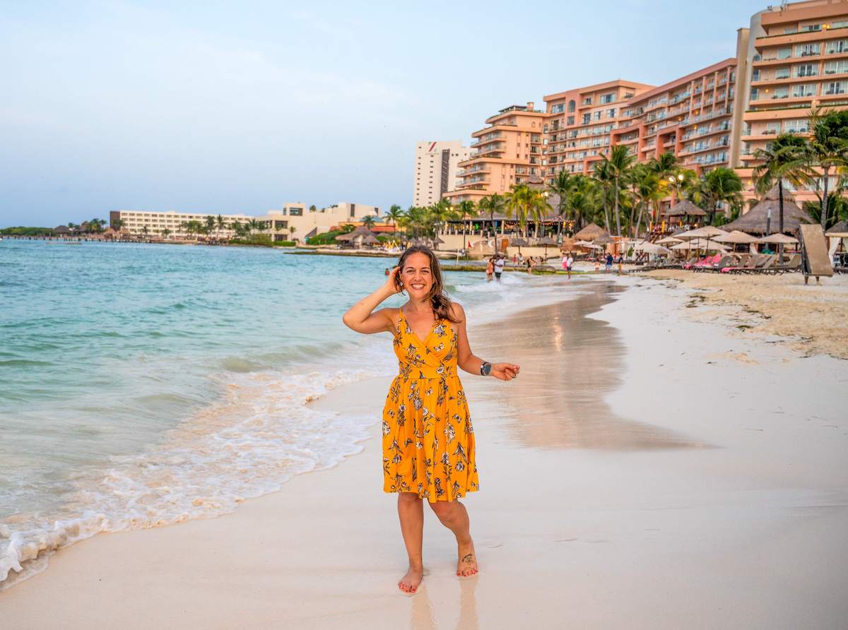 solo female traveler in a yellow dress walking along the beautiful beach in Cancun, Mexico