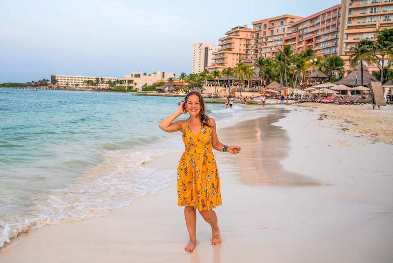 solo female traveler in a yellow sundress walking along the beach