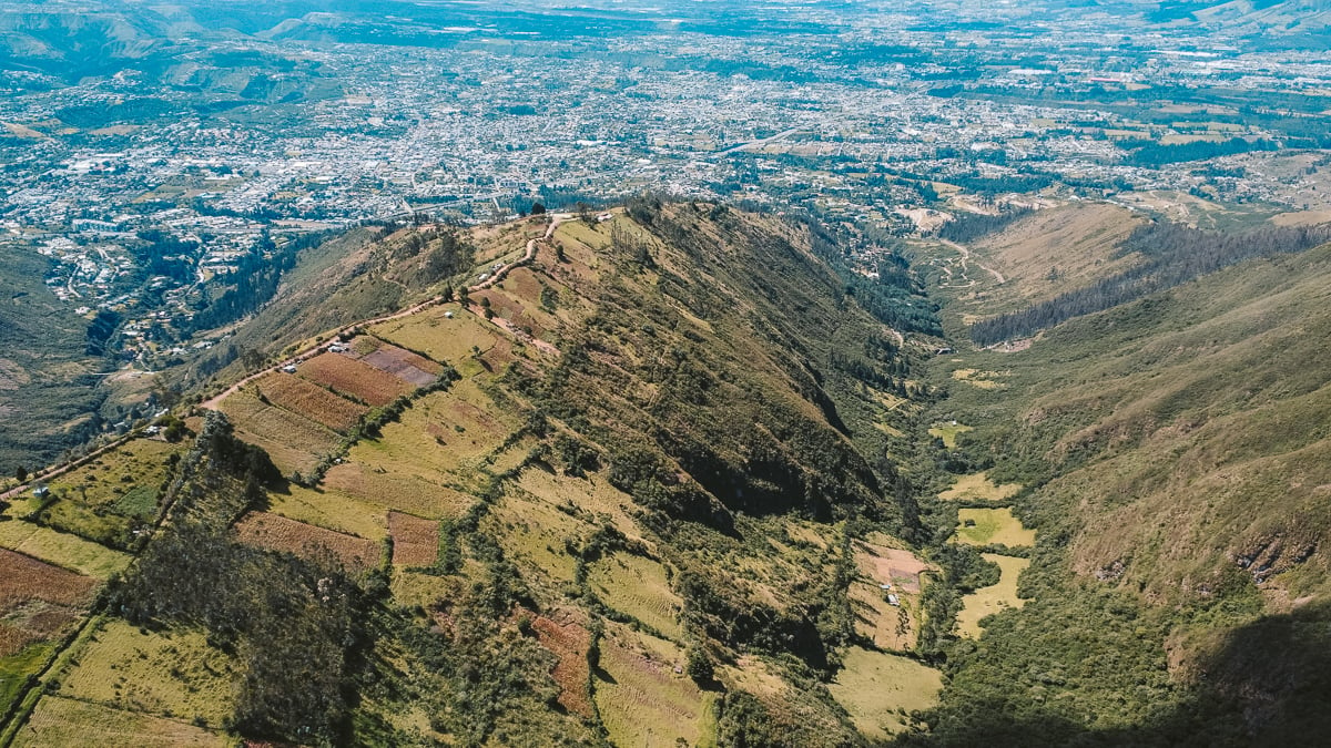 Drone shot from the top of Volcan Ilalo in Quito, showcasing a breathtaking aerial view of the lush green valleys and sprawling cityscape of Ecuador, perfect for an Ecuador solo travel itinerary.
