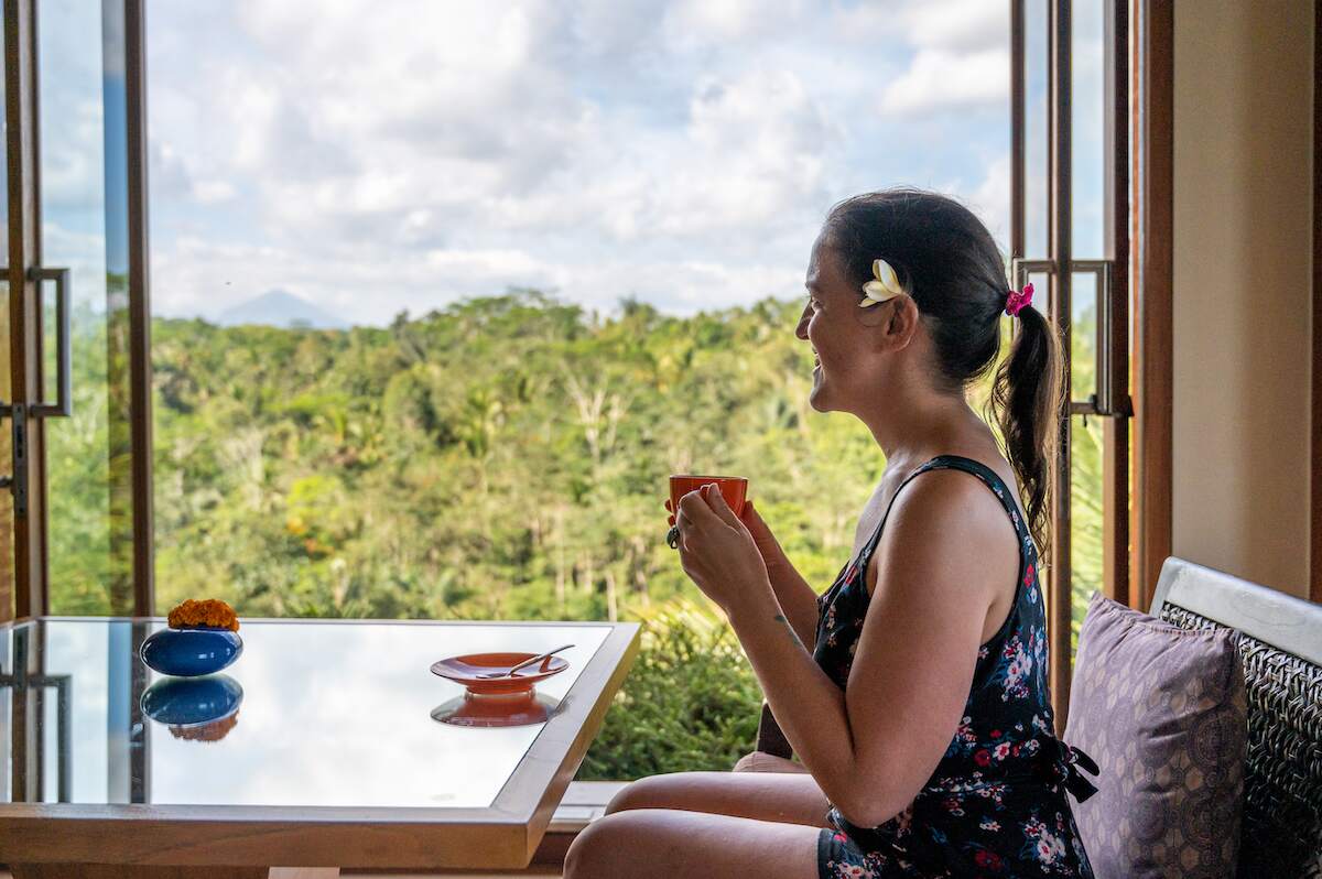 solo female traveler with a flower in her hair sipping coffee while gazing out over lush jungle from the rooftop lounge at Padma Resort Ubud in Bali