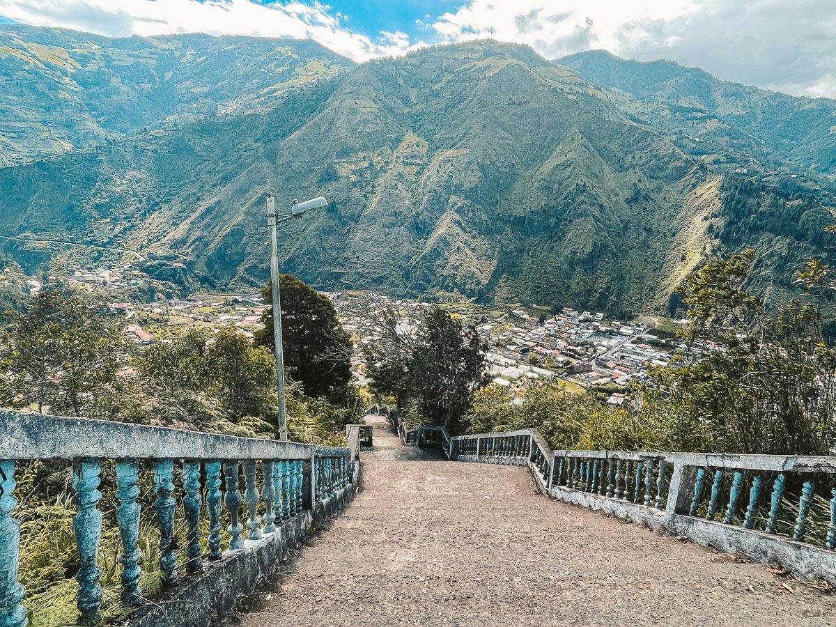 View from the stairs leading to La Virgen statue in Baños, Ecuador, with the town and lush green mountains in the background, offering a stunning perspective for solo travelers exploring the area.