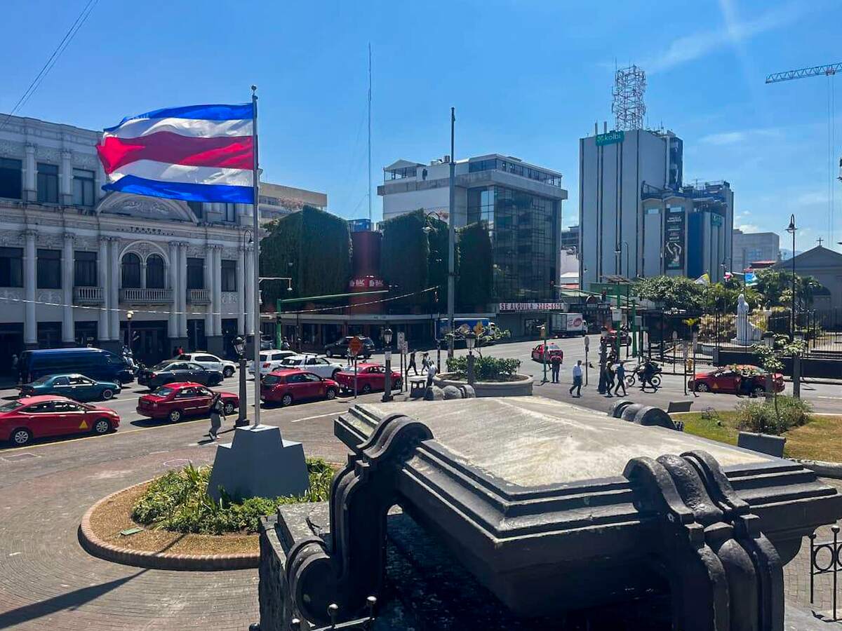 A busy street scene in San Jose, Costa Rica, with the national flag waving and buildings in the background, capturing the urban atmosphere as part of a vacation itinerary.