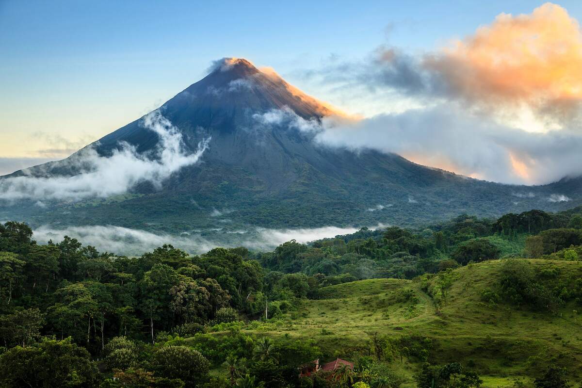 A breathtaking view of Arenal Volcano in Costa Rica, with its peak surrounded by clouds and lush green forest in the foreground, highlighting one of the key destinations in a 5 day Costa Rica itinerary.