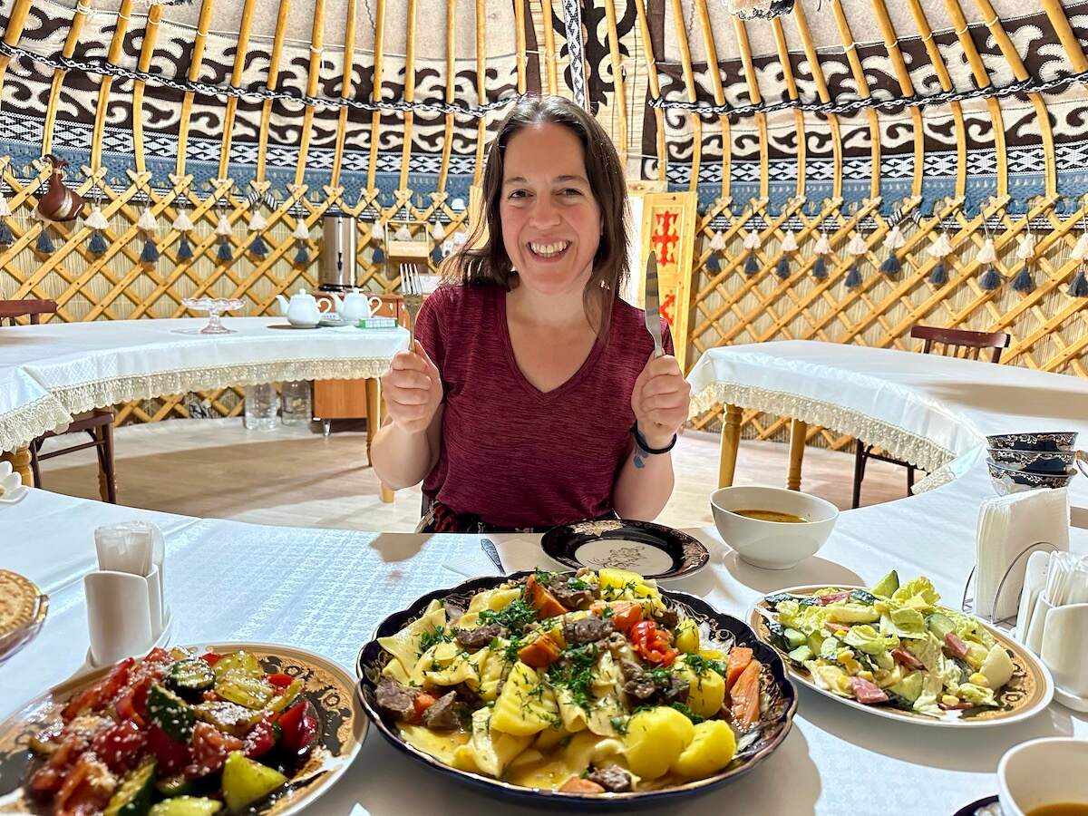 Enjoying a homemade dinner inside a traditional yurt at CBT Kazarman, featuring a variety of colorful dishes like beshbarmak and simple salad