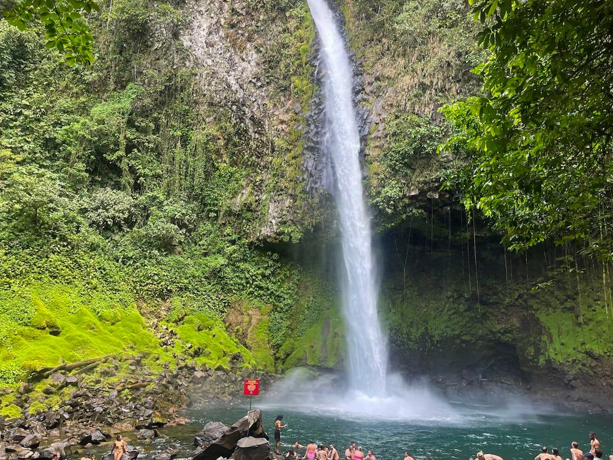 People swimming and relaxing at the base of La Fortuna Waterfall in Costa Rica, surrounded by lush greenery