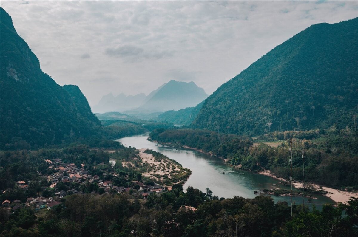 Panoramic view from Phanoi Viewpoint in Muang Ngoi, Laos, featuring a winding river surrounded by lush green mountains and a small village below, ideal for solo travelers seeking stunning vistas.