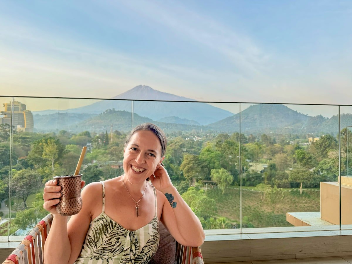 woman in a green dress holding a cocktail on the Gran Melia Arusha rooftop with a view of Mount Meru behind her