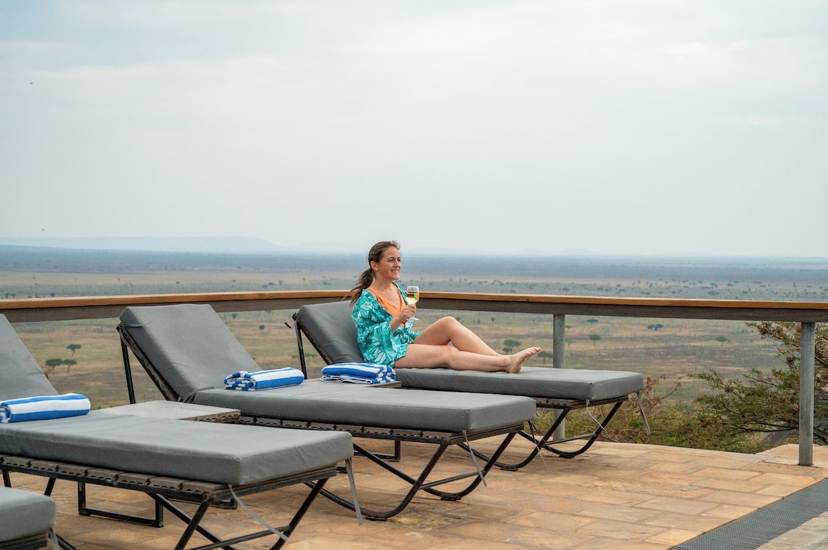 woman drinking a glass of white wine by the pool at Lahia Tented Lodge with the Serengeti behind her