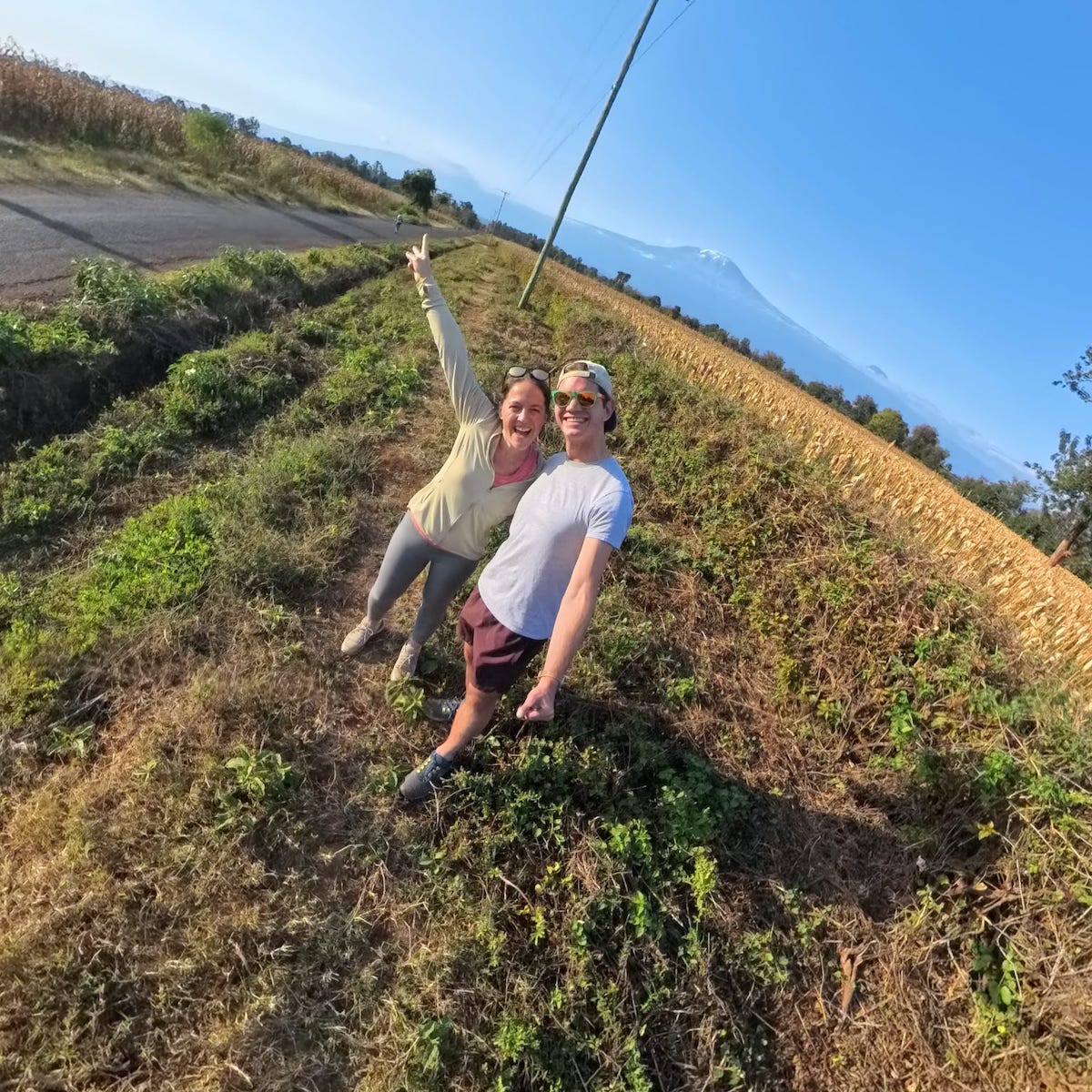 two travelers posing on the side of a road lined with corn fields in Moshi with Mount Kilimanjaro in the background