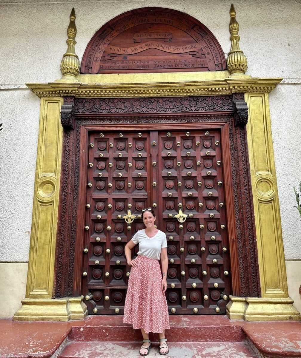 woman standing in front of an intricately-carved Indian-style door in Stone Town in Zanzibar