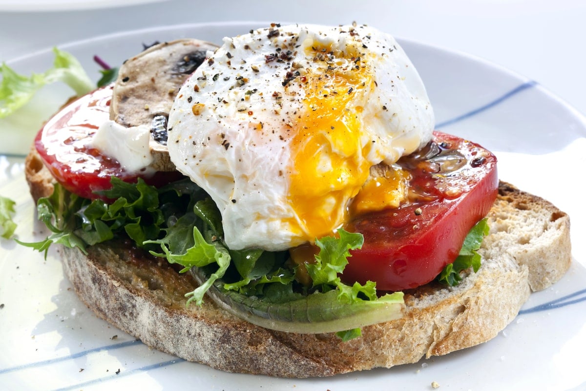 NYC brunch dish featuring a poached egg served on thick bread with fresh lettuce and tomato