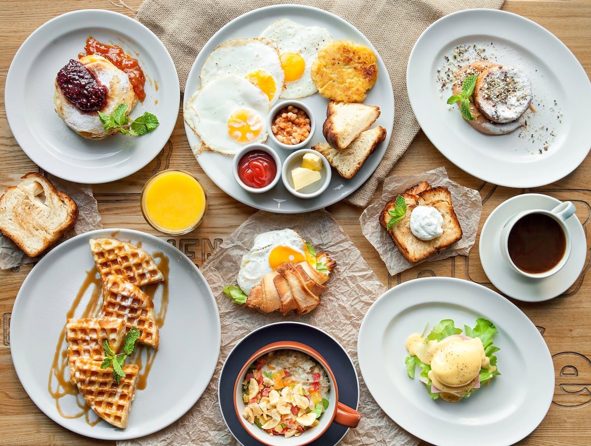 Assorted NYC brunch dishes on a table, including waffles, eggs benedict, oatmeal, coffee, toast, and brioche.