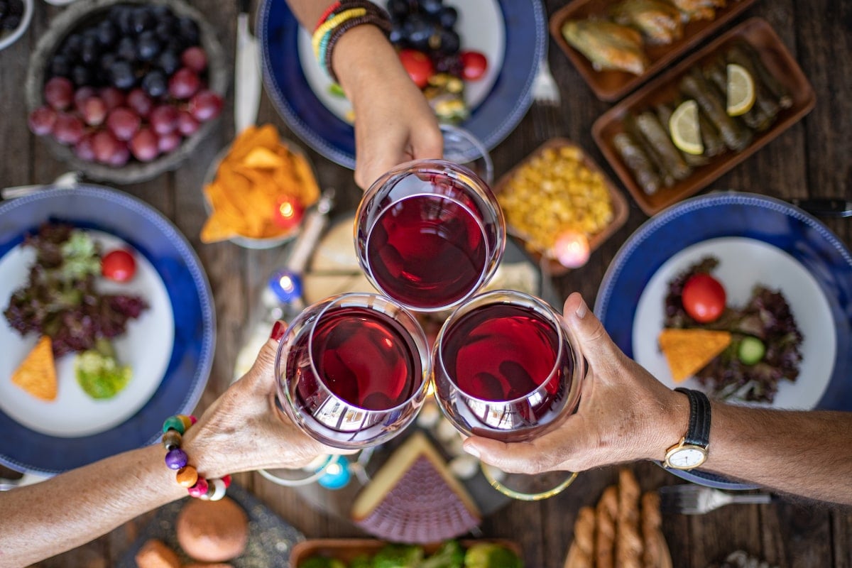 friends at a weekday boozy brunch in NYC clinking glasses of red sagria over plates of salad, nachos, and other dishes