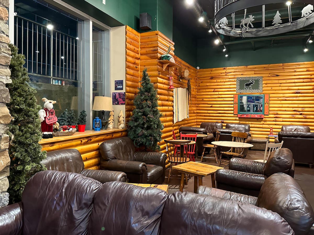 Interior of Cabin Coffee in Halifax, featuring rustic log cabin walls, leather couches, small pine trees, and cozy seating areas with warm lighting.