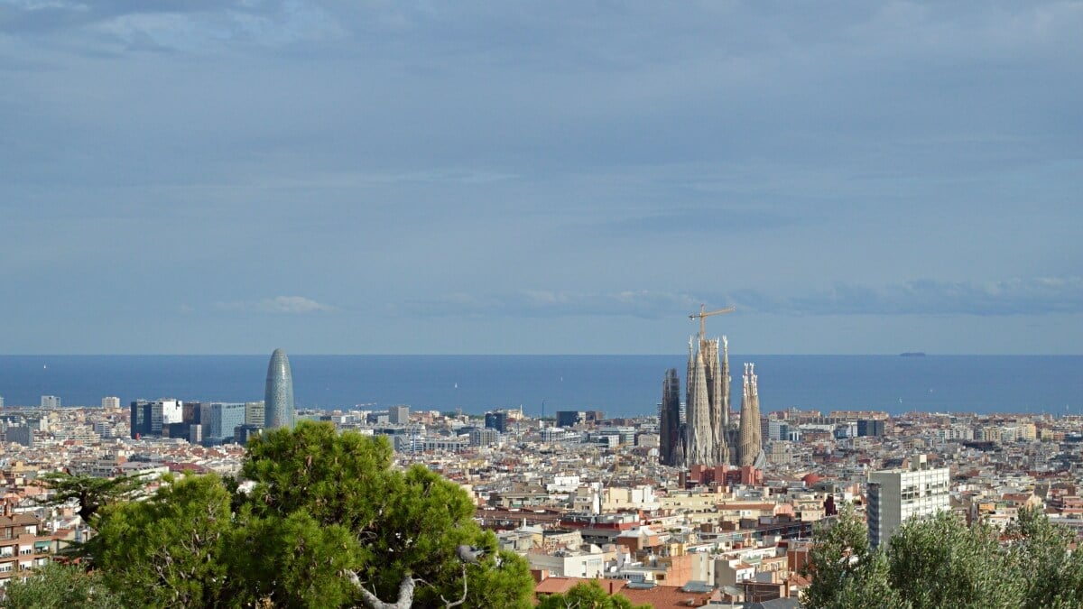 Expansive view over Barcelona from Park Güell, with the Sagrada Família and Torre Glòries standing out against the cityscape and the Mediterranean Sea in the background.