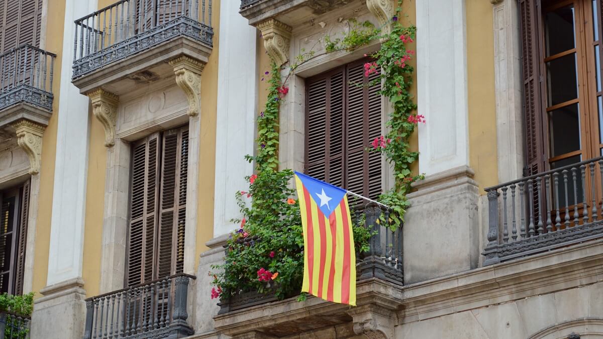 Catalan flag displayed on a balcony in Barcelona, with surrounding greenery and blooming flowers adorning the building’s traditional architecture.