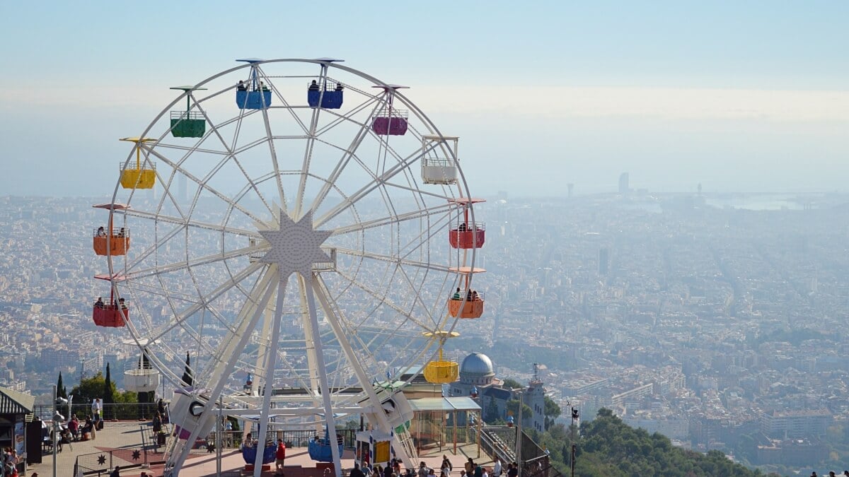 View over Barcelona from Mount Tibidabo, with a colorful Ferris wheel from Tibidabo Amusement Park in the foreground, offering a playful contrast to the expansive cityscape below.