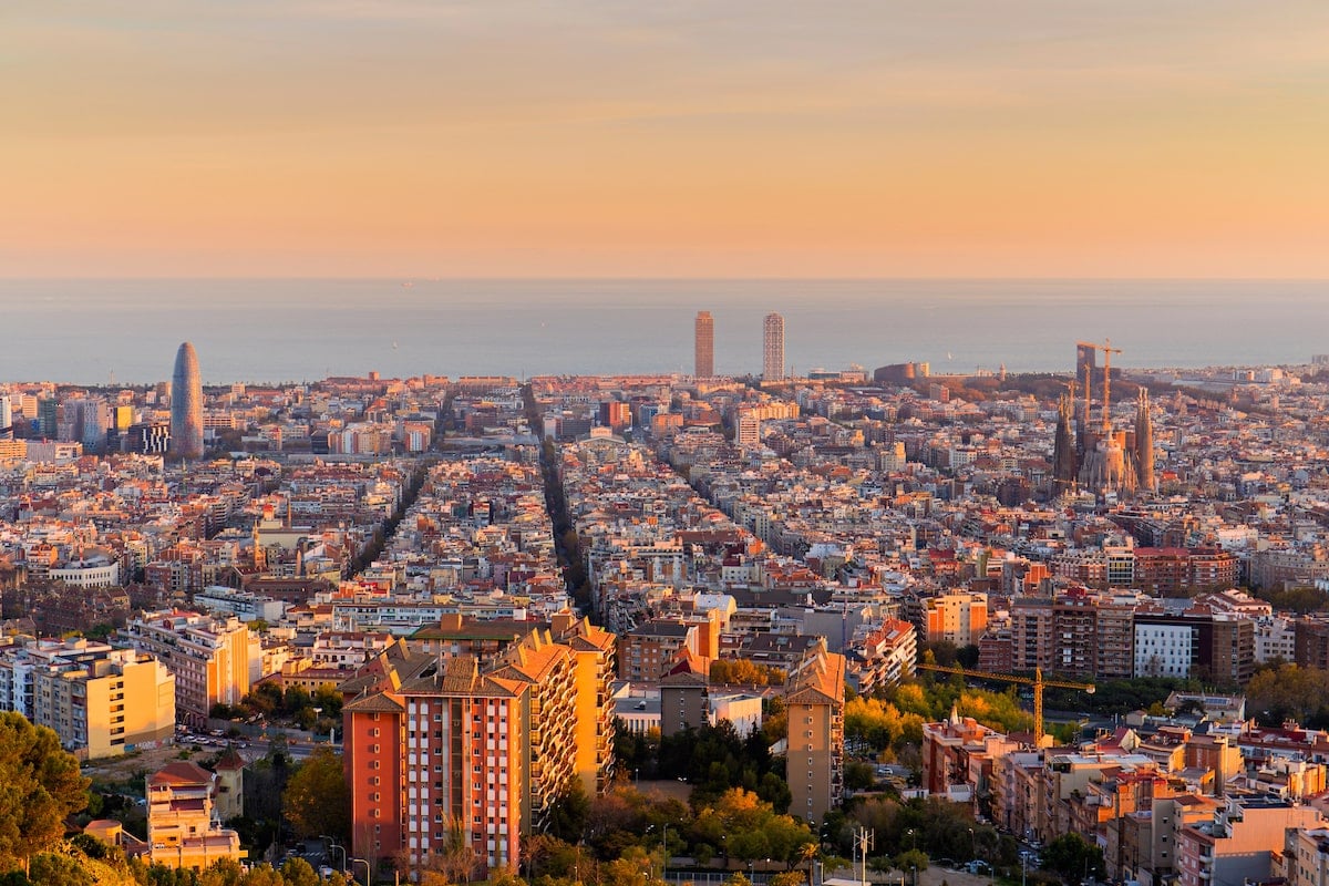 Barcelona skyline bathed in golden hour light, with iconic landmarks like the Torre Glòries and Sagrada Família standing out against the Mediterranean Sea in the background.