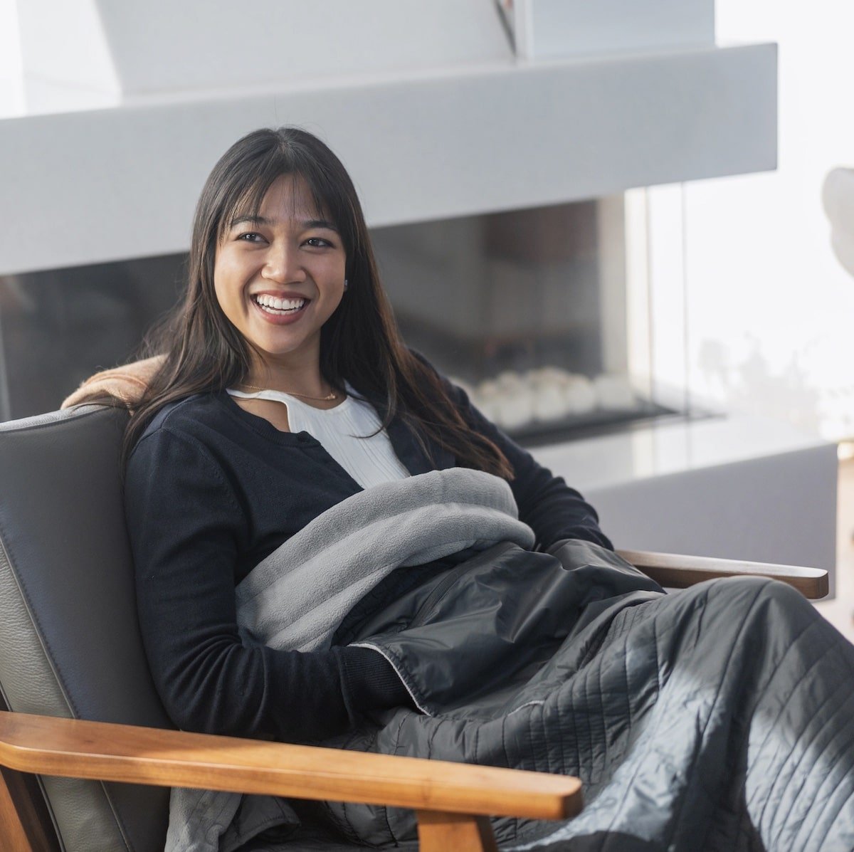 solo female traveler sitting in a hotel room staying warm while wearing the Explorer Travel Blanket from Puffer Hug