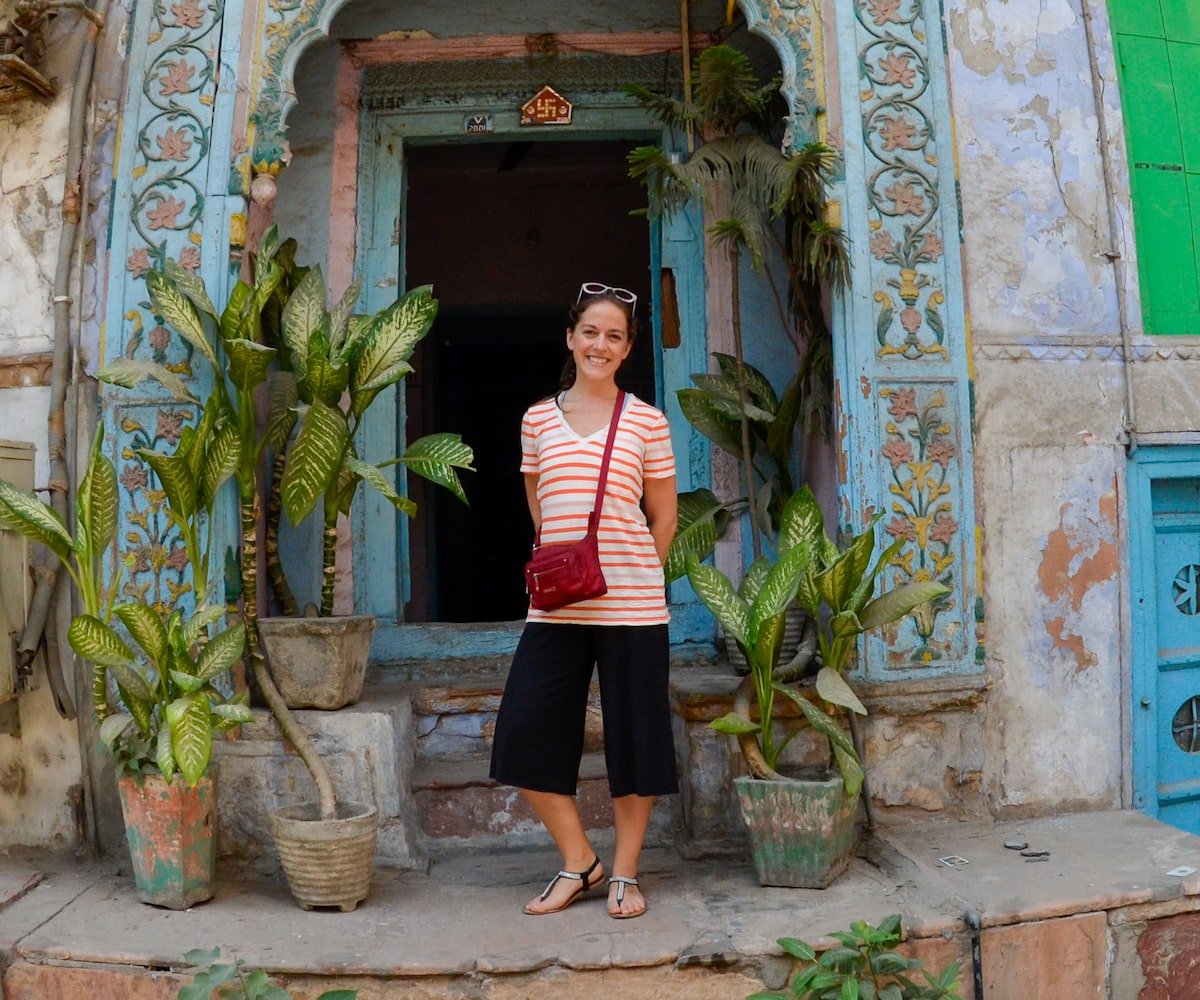 solo female traveler in Mumbai standing in front of a doorway with floral trim and plants on the stoop