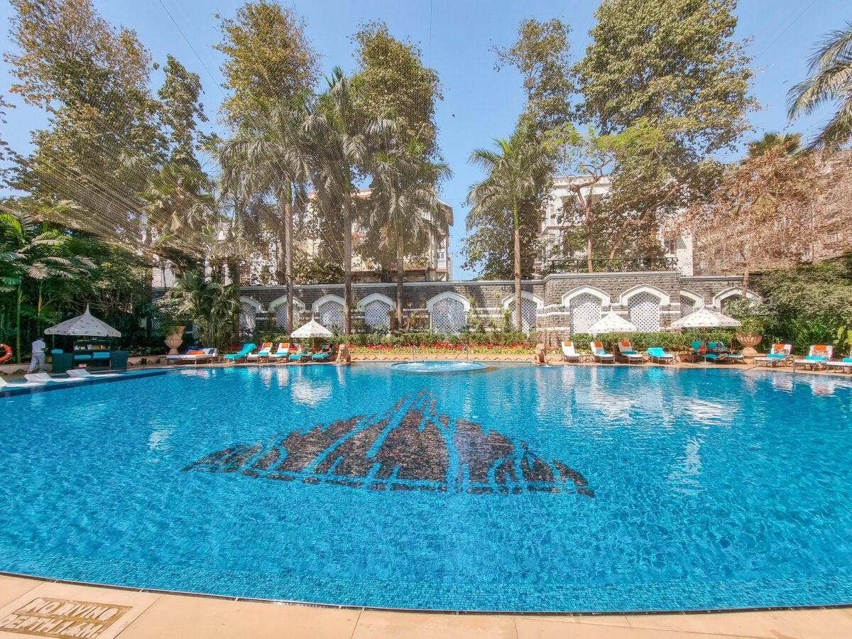 Swimming pool at the Taj Mahal Palace Hotel in Mumbai, surrounded by lush greenery, ornate white arches, and poolside lounge chairs, offering a luxurious and tranquil escape.