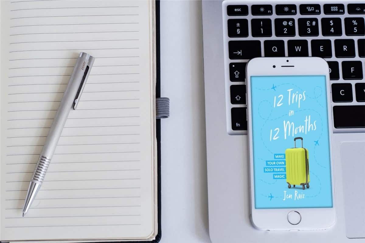 travel blogger planning out the cover art of her travel memoir on her phone with a notebook sitting next to it