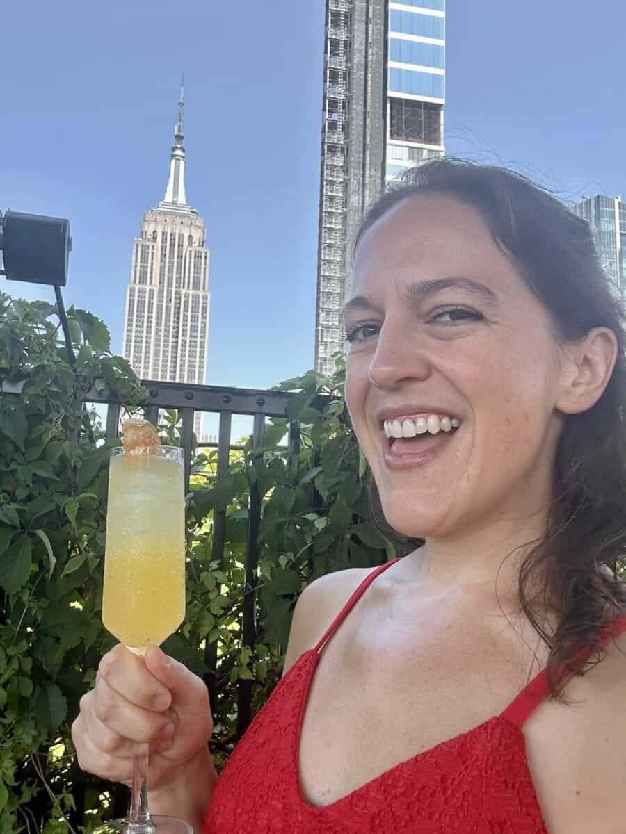 woman in a red dress sipping a mimosa during boozy brunch at 230 Fifth in NYC with a view of the Empire State Building in the background