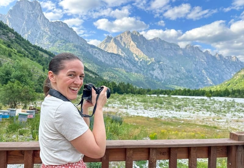 female travel photographer in a white t-shirt and pink skirt taking pictures of Albania's mountains