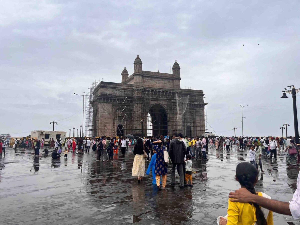 Street-level shot of the Gateway of India, bustling with tourists and vendors. The angle emphasizes the arch and the cobbled plaza.