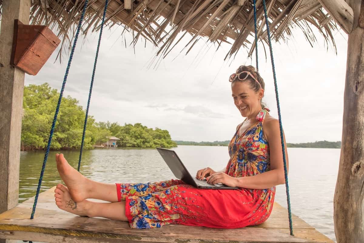 female travel blogger in a red dress typing on her laptop while working on her digital products