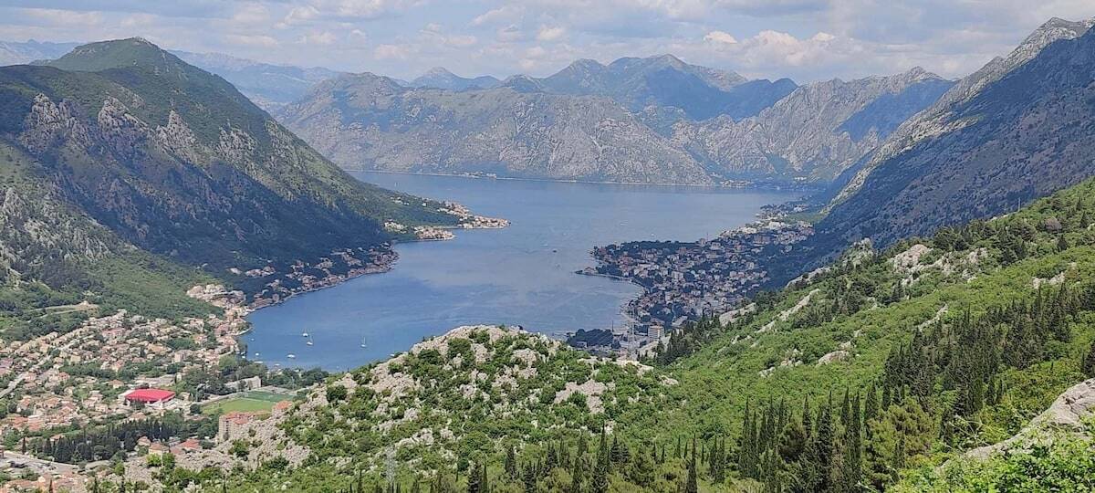 Panoramic view of the Bay of Kotor in Montenegro, with fjord-like blue waters surrounded by steep green mountains and coastal towns along the shoreline.
