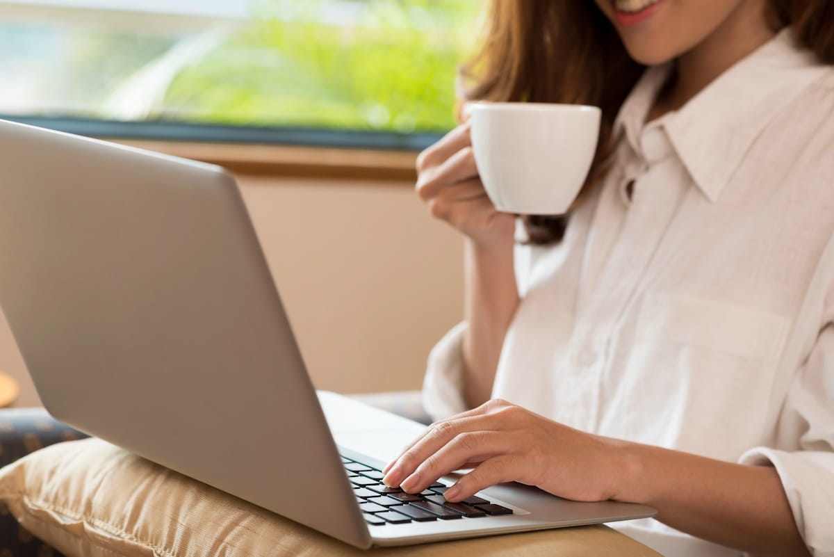blogger in a white shirt holding a cup of coffee while typing on her laptop