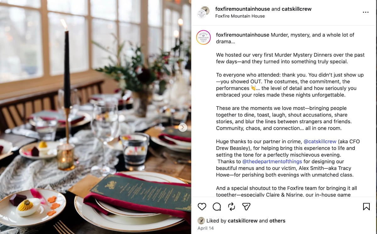 An Instagram post from Foxfire Mountain House, in collaboration with Catskill Crew, showcases a beautifully set long wooden dining table ready for a Murder Mystery Dinner. The table is decorated with a lace runner, greenery, tall black taper candles, and individual place settings featuring gold-rimmed plates and dark green menus. The accompanying caption thanks those who attended for their commitment to the roles and costumes, while giving a special shoutout to @catskillcrew for partnering to help bring the community-focused event to life.