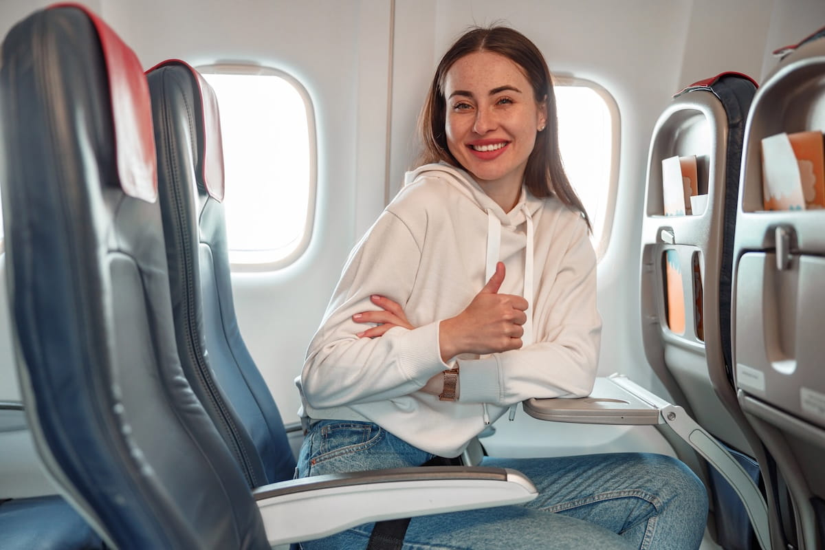 women flying solo for the first time sitting in airplane seat and giving a thumbs up while smiling at the camera