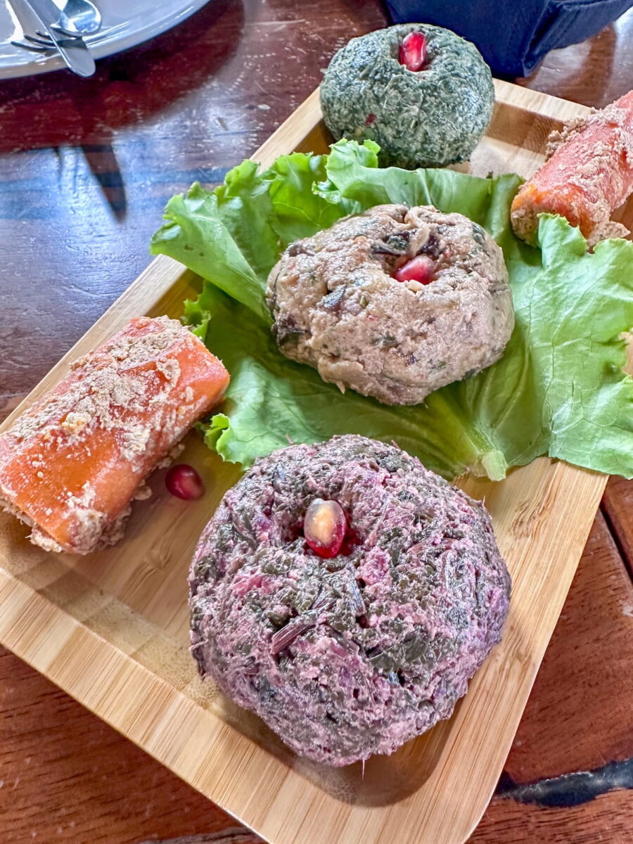 A close-up of a traditional Georgian pkhali platter at Restaurant Kvamli, featuring colorful minced vegetable and walnut spreadsโincluding spinach, beetroot, and eggplantโshaped into small mounds on lettuce leaves and garnished with bright red pomegranate seeds.