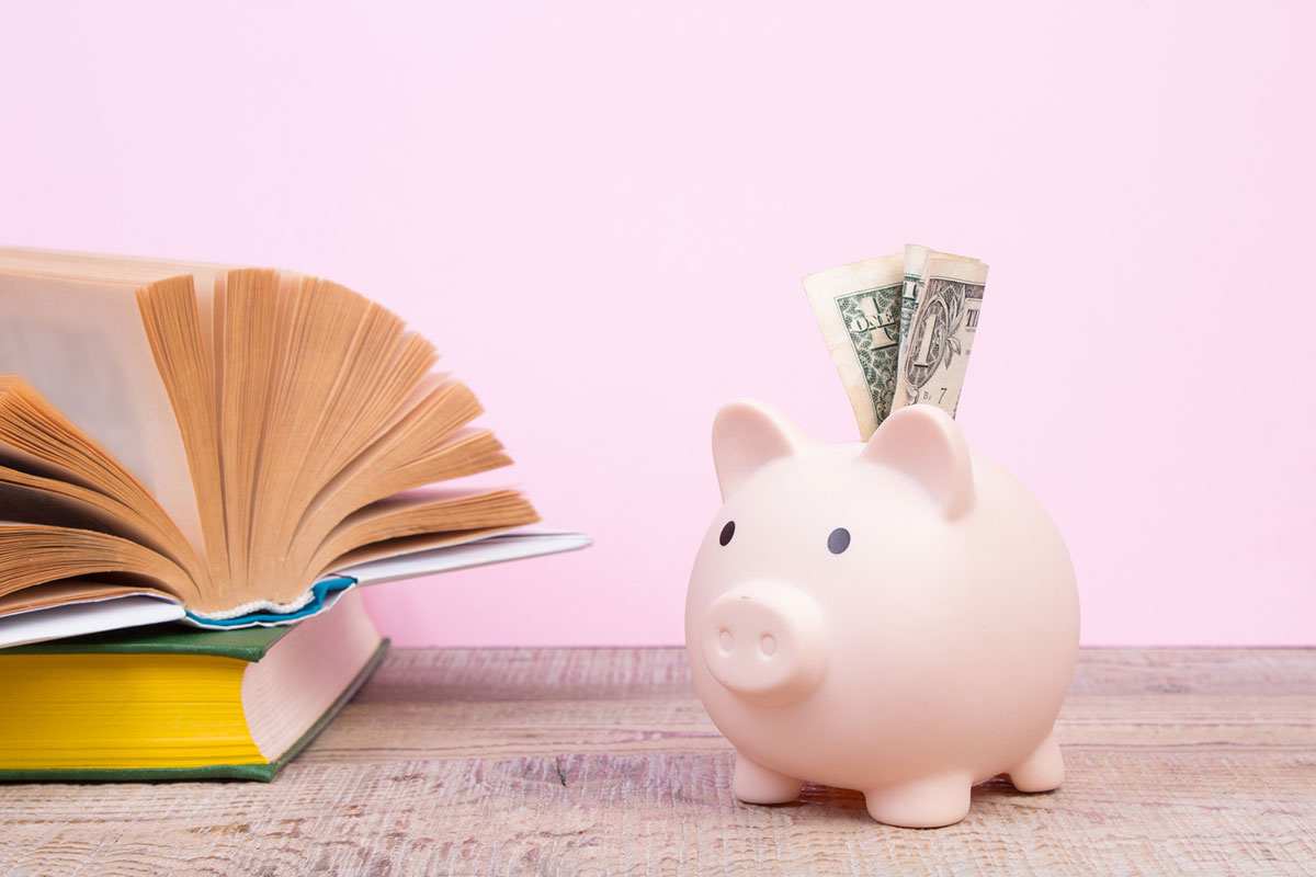 Piggy bank with notes and investing books on pink background.