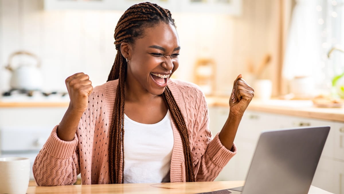 Woman cheering at her laptop computer while sitting in her kitchen doing a Preply language lesson.