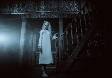 ghost-like figure walking down the stairs of a haunted hotel