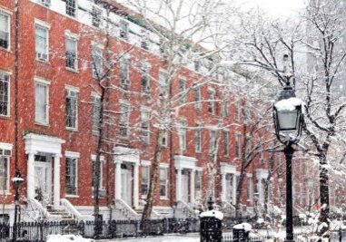 Snow covered winter street scene with old buildings along Washington Square Park.
